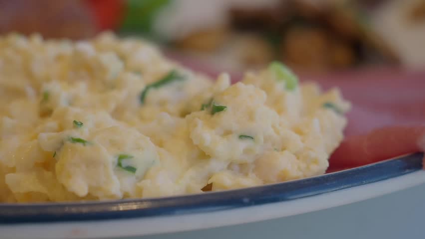 Soft focus motion of creamy scrambled eggs with chives served on a colorful plate with ham slice.