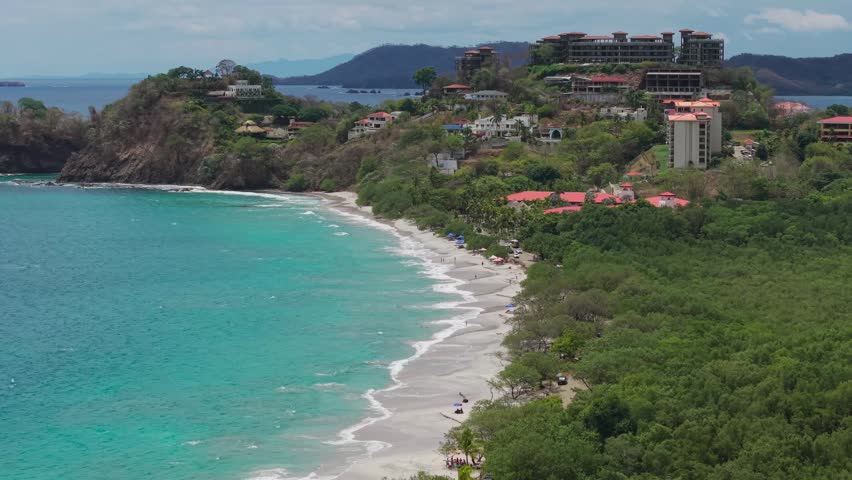 Drone Pan left aerial view of Playa Flamingo with turquoise water and coastal houses in Costa Rica.