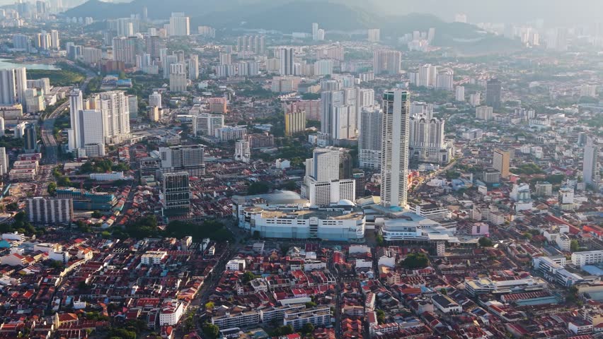 Close up aerial shot of George Town, Penang Island, with KOMTAR Tower in Malaysia. Dense cityscape with high-rise buildings and mountains in the background under soft daylight. UHD.