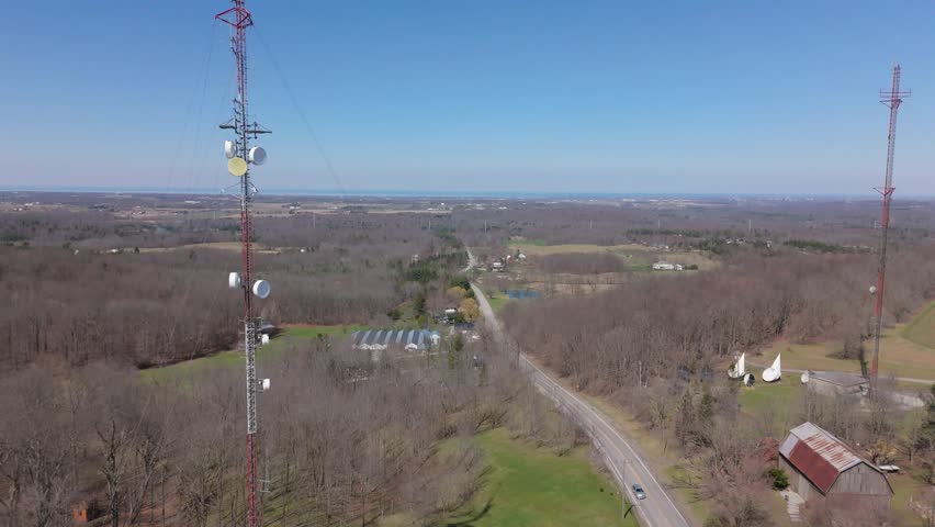 Rising drone shot of radio tower with rolling hills, trees, and horizon in the distance.