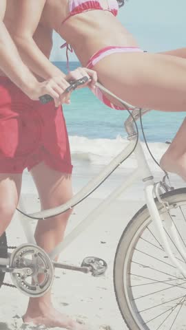Vertical video: Man steadying bike as woman shifting seat, camera zoom showing overlays travel tone. Couple, beach, romance, laughter, bicycle, sunny, vertical video