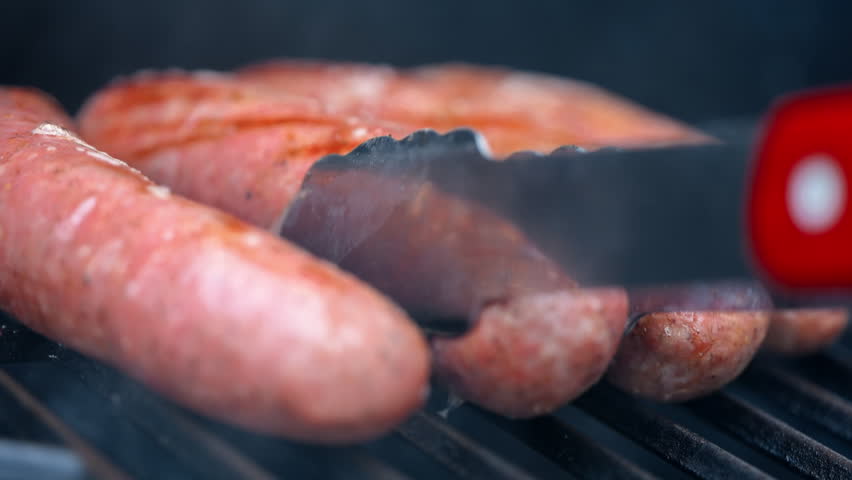 Close up shoot of Sausages grilling on barbecue with open flame. Close up of juicy meat cooking on grill, outdoor food and summer barbecue