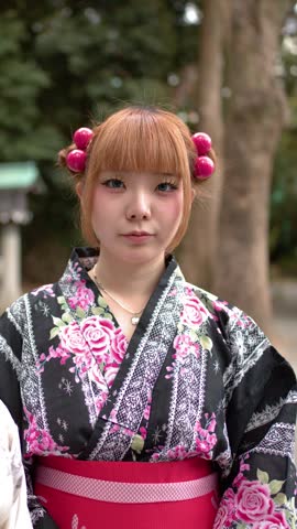 Two women in traditional kimono stand smiling before a wooden torii gate in Tokyo