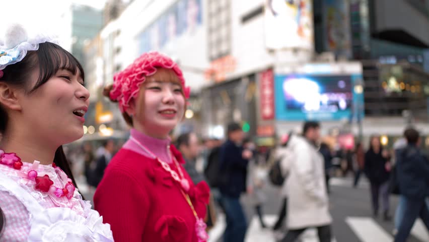Two women wearing colorful Decora street style pose and smile in busy Shibuya Crossing, Tokyo
