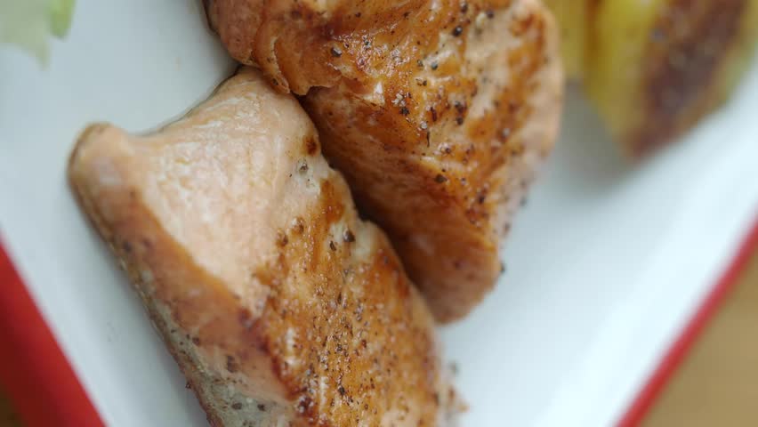 Close up view of cooked salmon steak served with seasoned roasted potatoes and fresh lettuce garnish slow pan footage.