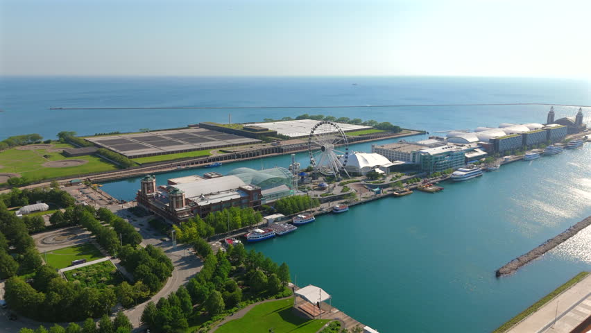Stunning aerial view of Chicago Navy Pier featuring iconic ferris wheel and Lake Michigan waterfront. Boats dock along pier while green parks and historic buildings create a vibrant urban landscape.