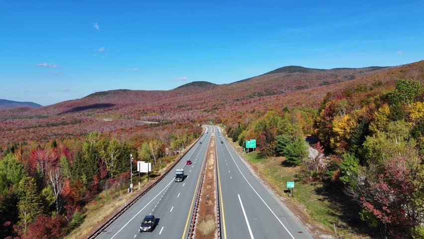 Straight 93 highway road with traffic cutting through colorful autumn White Mountain National Forest from above, New Hampshire, US