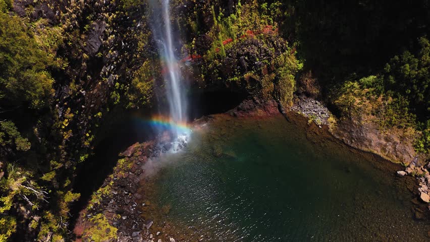 Aerial view of waterfall creating rainbow over natural pool in Madeira