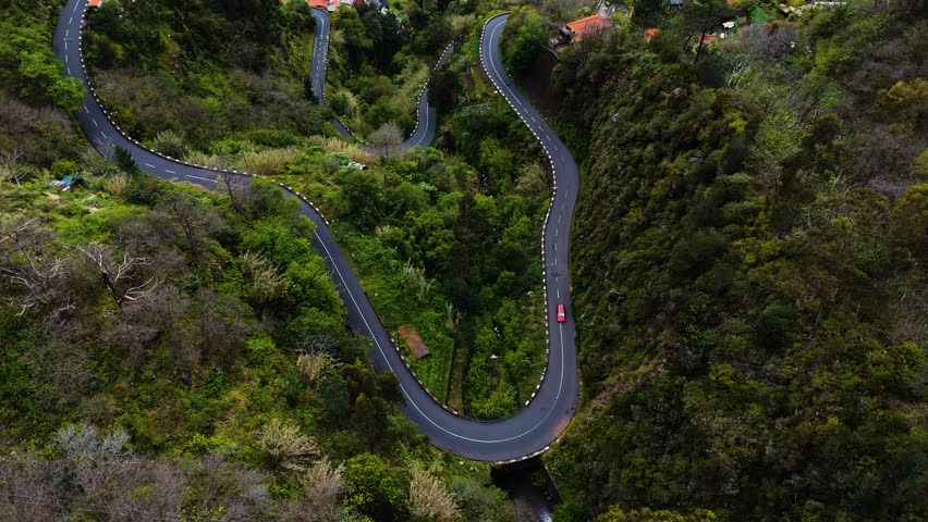 Top view aerial descending toward red car driving on winding road in Madeira