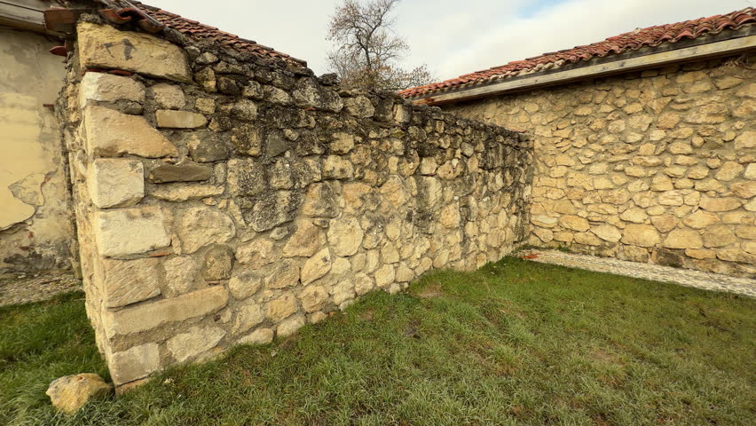 A long stone building with a red tiled roof stands on a grassy field. The rough walls and bare trees create a calm, nostalgic feeling. This peaceful scene captures the quiet beauty of a cold morning.