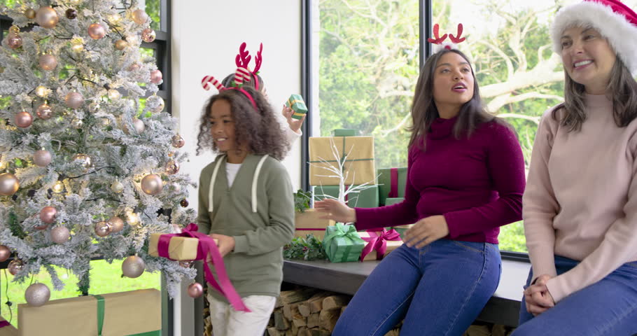 Diverse family exchanging gifts by Christmas tree in living room celebrating holiday morning. Festive, celebration, warmth, togetherness, cozy, joyful, holiday