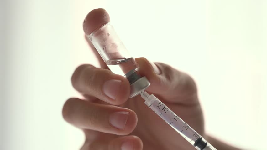 Medical professional aspirating medicine from a glass vial into a syringe against a white background