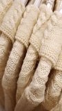 Cream-colored cable-knit sweaters hang in a row on white hangers. Close-up pan shot reveals the soft, fuzzy texture of the warm wool fabric and detailed stitching. - Powered by Shutterstock - Get 15% off with code: PIKWIZARD15