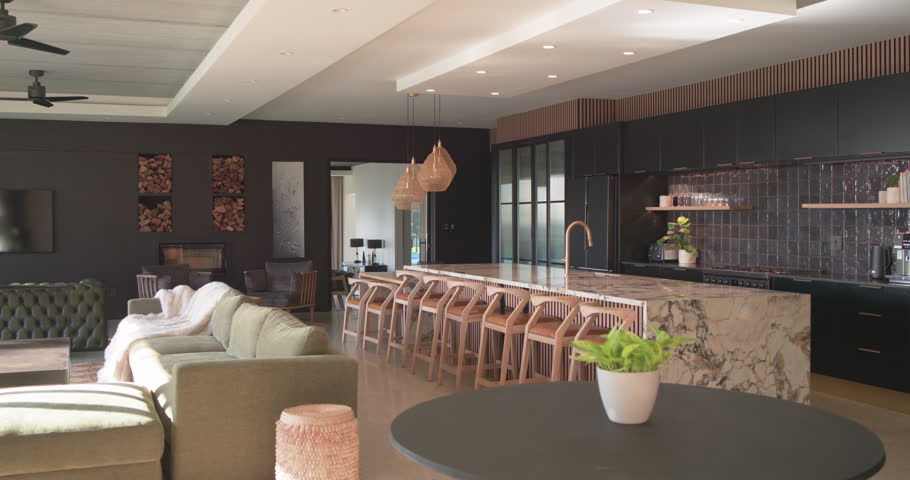 Camera starting near table, panning left and showing marble island, bar stools in open-plan kitchen. Countertop, modern, minimalist, stone, wood, pendant, greenery