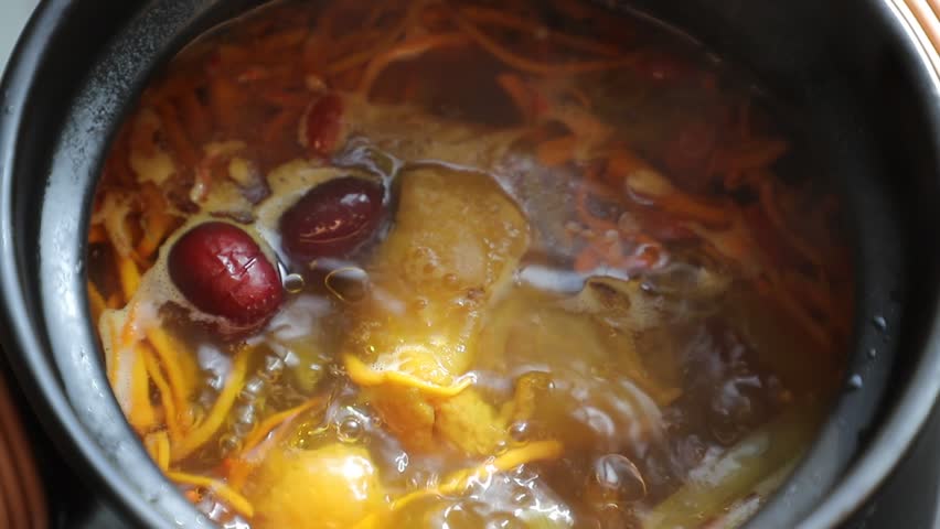 Close-up shot of simmering homemade chicken soup with mushroom, red dates and goji berries. Hot nutritious healthy tonic broth steaming in cooking pot, warm traditional Chinese cuisine cooking 