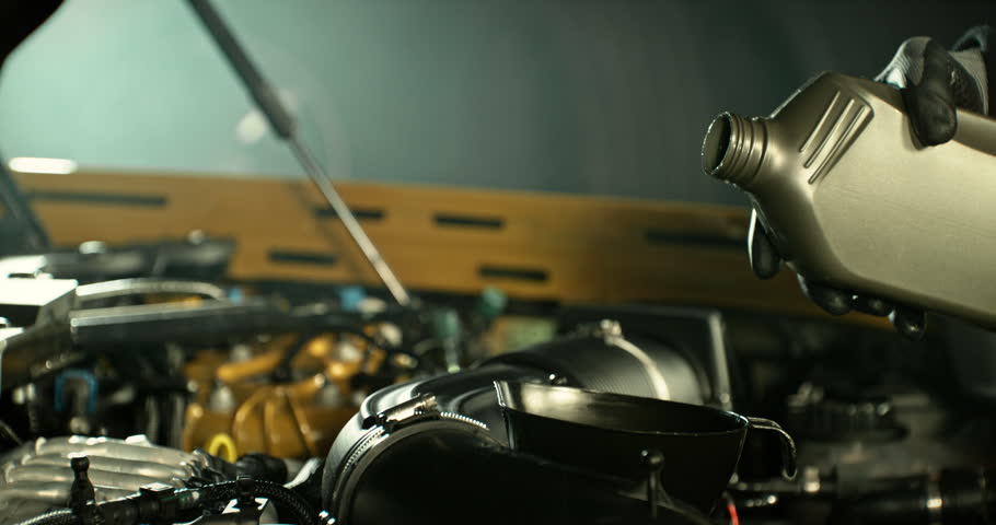 Super slow motion shot of pouring motor oil into car engine with camera movement around bottle neck. Automotive maintenance concept, lubrication, service and repair.