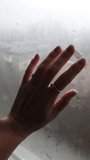 Female hand touches and wipes condensation off a wet windowpane, revealing a gloomy city view outside. The scene has a melancholic and lonely mood with soft, natural light filtering through the fogged - Powered by Shutterstock - Get 15% off with code: PIKWIZARD15