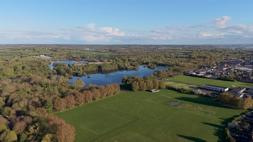 Drone flight over Nightleys Playing Field, Cheshunt, moving forward on a blue sky day with Turnford School buildings and Lee Valley Regional Park lakes and woodland behind.