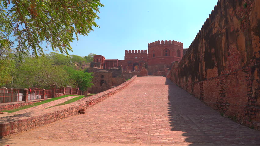 A wide static shot of the monumental red sandstone defensive walls and the stone-paved entrance ramp leading into the historic city of Fatehpur Sikri under a clear sky.