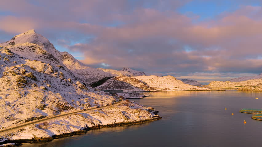 Breathtaking drone shot of snowcovered mountains and arctic fjords in Lofoten, Norway, during a vibrant sunset. Captures the authentic beauty of the Nordic landscape.
