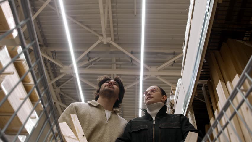 Couple pushes shopping cart forward browsing goods in hardware store from cart view. They stroll aisle studying shelves under high ceiling