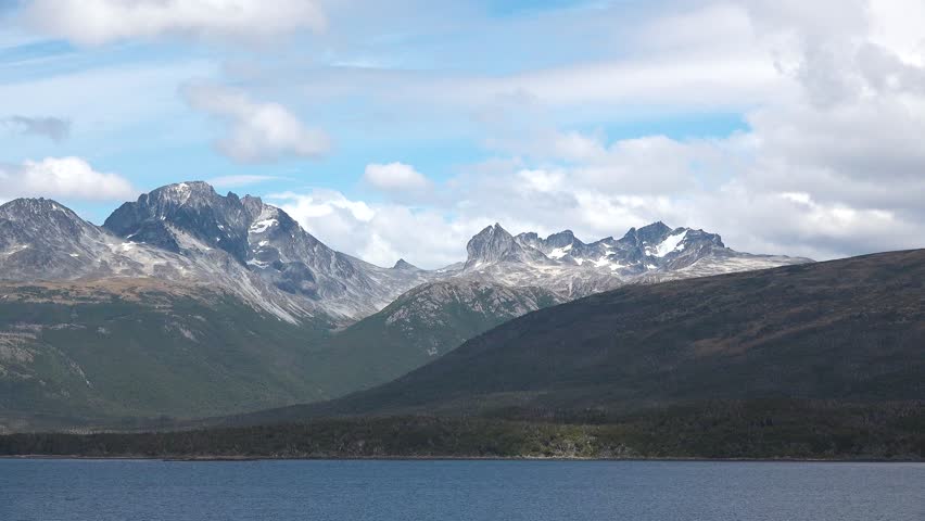 The camera shows a landscape with mountains rising above a body of water. The setting is near Ushuaia, Argentina, with clouds overhead during the daytime.