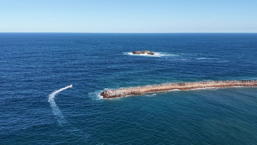 Aerial View of Boat Near Ocean Breakwater, Stunning aerial view of a small island surrounded by crashing blue waves.