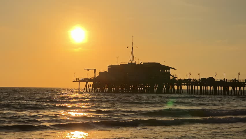 Santa Monica Pier silhouette over Pacific Ocean at sunset, shimmering water with golden reflections and calm coastal evening atmosphere
