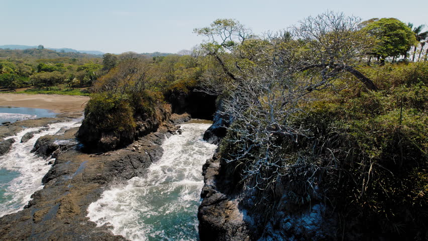 Coastal waves hitting rocky shore with pelicans on tropical beach in Costa Rica