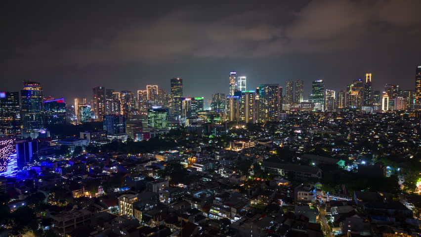 Aerial night timelapse of Jakarta skyline with illuminated skyscrapers and glowing city lights. Urban cityscape showing modern architecture and metropolitan life in Indonesia.