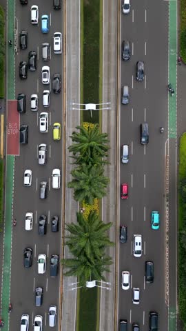 Aerial top-down view of busy multilane street with traffic and motorbike lanes in central Jakarta, Indonesia. Urban transportation scene with cars, palm trees, and road infrastructure.