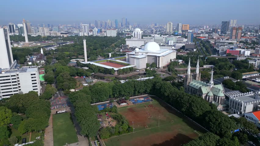 Aerial view of Istiqlal Mosque in Jakarta with surrounding park and skyline. Wide cityscape showing modern architecture, urban layout and cultural landmark in Indonesia.