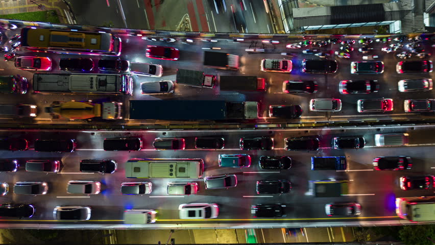Top-down aerial timelapse of night traffic in Jakarta, Indonesia. Dense cars and vehicles with headlights and taillights on busy multilane urban road showing city transport and congestion.