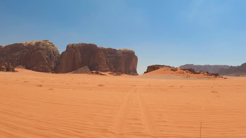 Aerial view of red sand dunes and sandstone rock formations under a clear sky within the desert of Wadi Rum, Jordan.