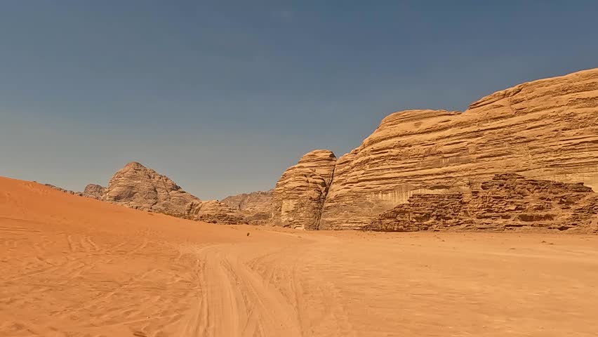 Aerial view of red sand dunes and massive sandstone rock formations with tire tracks leading through the desert valley in Wadi Rum, Jordan.
