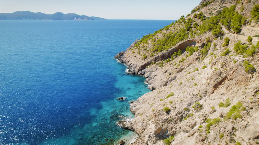 Rocky shoreline and clear blue sea water viewed from a winding cliff road in Greece