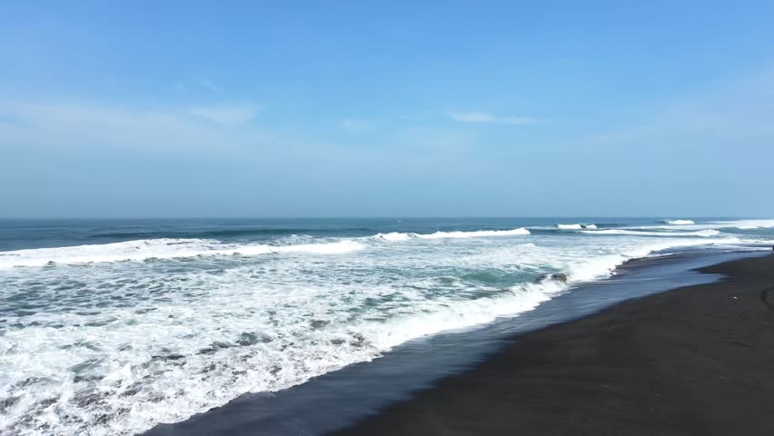 A video of crashing waves in south coast of central java indonesia. Aerial view of Dewa Ruci beach of Purworejo. Beach waves, sand, under the blue sky