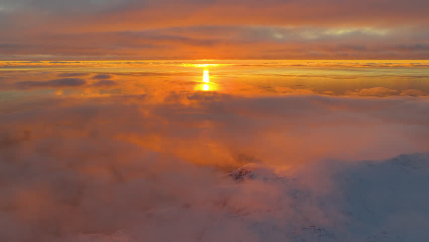 Breathtaking aerial view of a golden hour sunset reflecting on a sea of clouds above the snowcapped peaks of Lofoten, Norway.