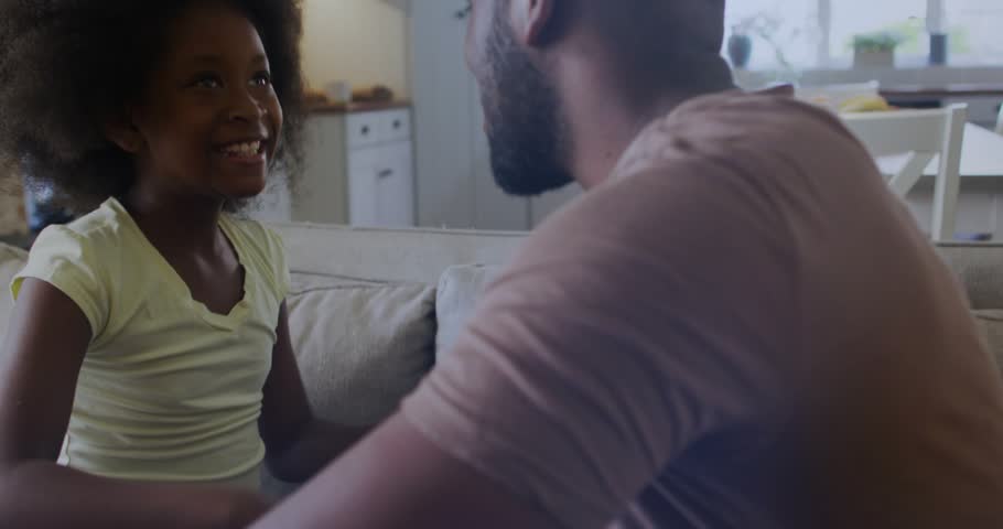 Girl reaching forward hugging dad on couch, overlaying HUD circles and code, showing joy amid tech. Daughter, father, family, affection, embrace, sofa, livingroom