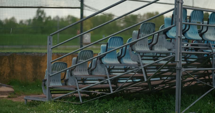 Close-up of empty metal bleachers with rows of plastic seats beside a fenced outdoor area.