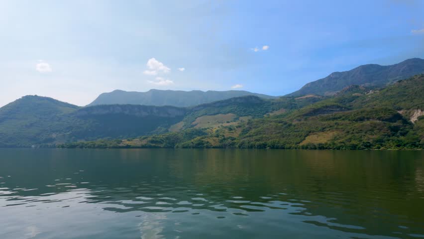 A smooth tracking shot from a boat showing the vibrant green vegetation and the high mountain ridges surrounding the Grijalva River in the Sumidero Canyon National Park, Chiapas.