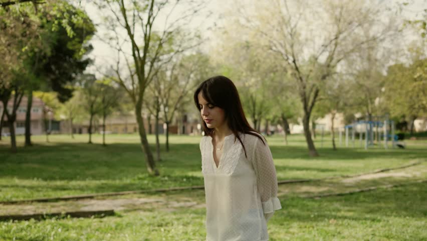 Young woman standing alone reflecting in a sunny park