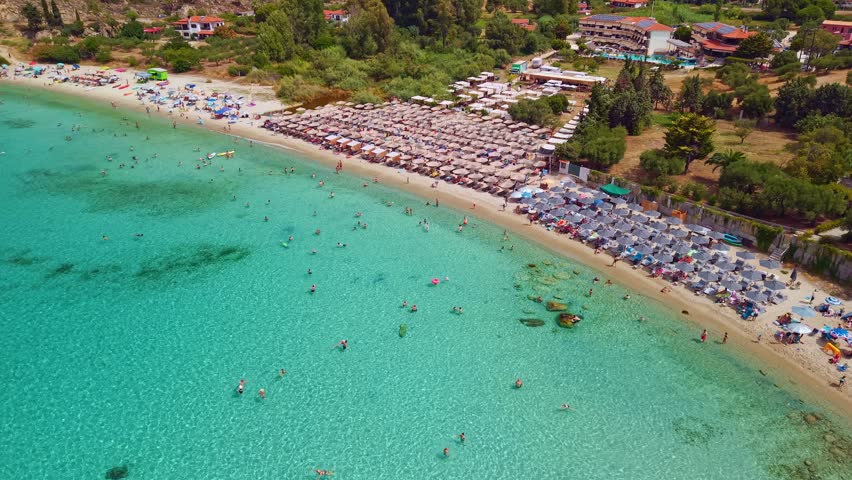 High angle drone perspective of the small Koviou beach featuring crystal clear turquoise water and lush green hills in Sithonia, Chalkidiki, Greece