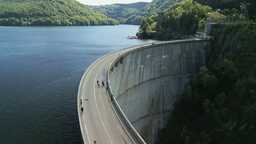 Aerial view of Vidraru Dam with concrete arch wall and cars on top on the Transfagarasan mountain road at summer in Romania