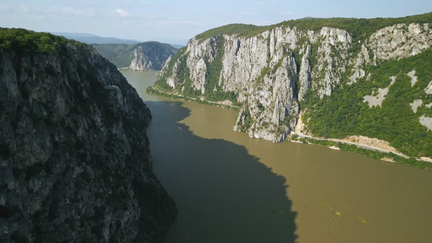 Aerial view flying forward through the Iron Gates gorge on the Danube river with dramatic limestone cliffs and lush green mountains at the border of Romania and Serbia