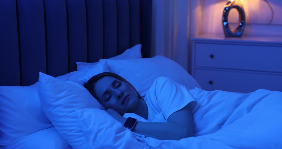 Woman with sleep tracker sleeping on bed at home. Camera moving forward