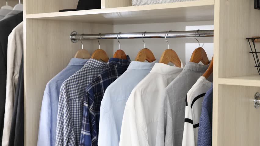 Man putting hanger with shirt into wardrobe indoors, closeup