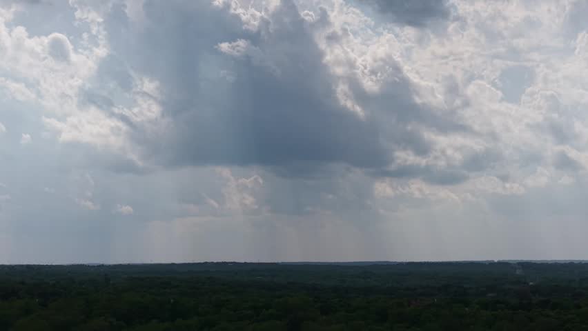 Drone aerial push forward toward rain shafts falling from storm clouds over a forest landscape in Oklahoma during spring.