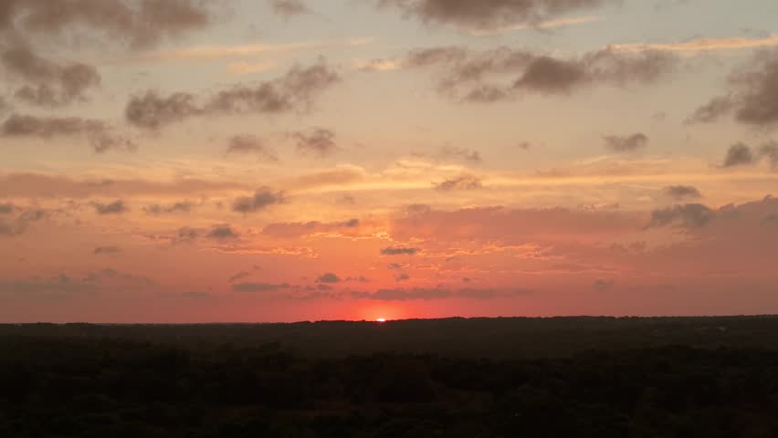 Drone aerial push forward as sun dips below horizon over forest landscape in Oklahoma at sunset.