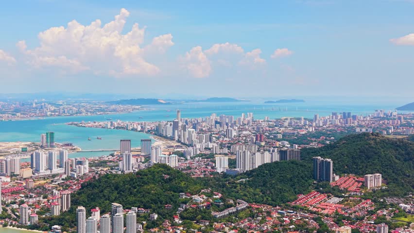 Zoomed in drone shot of Pulau Penang Island, Malaysia. Features George Town skyline, lush tropical hills, and the turquoise Andaman Sea with the Penang Bridge in the background. UHD.